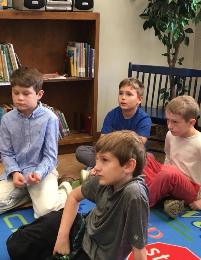 Four children sitting on a rug in a classroom