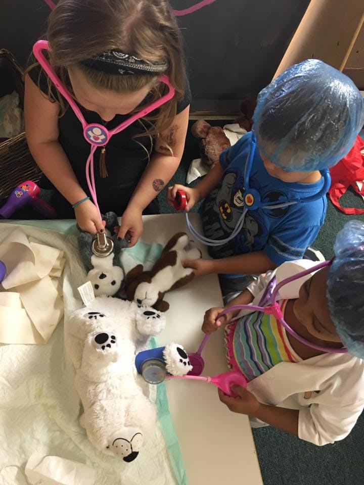 Three children playing with toy medical equipment and stuffed animals