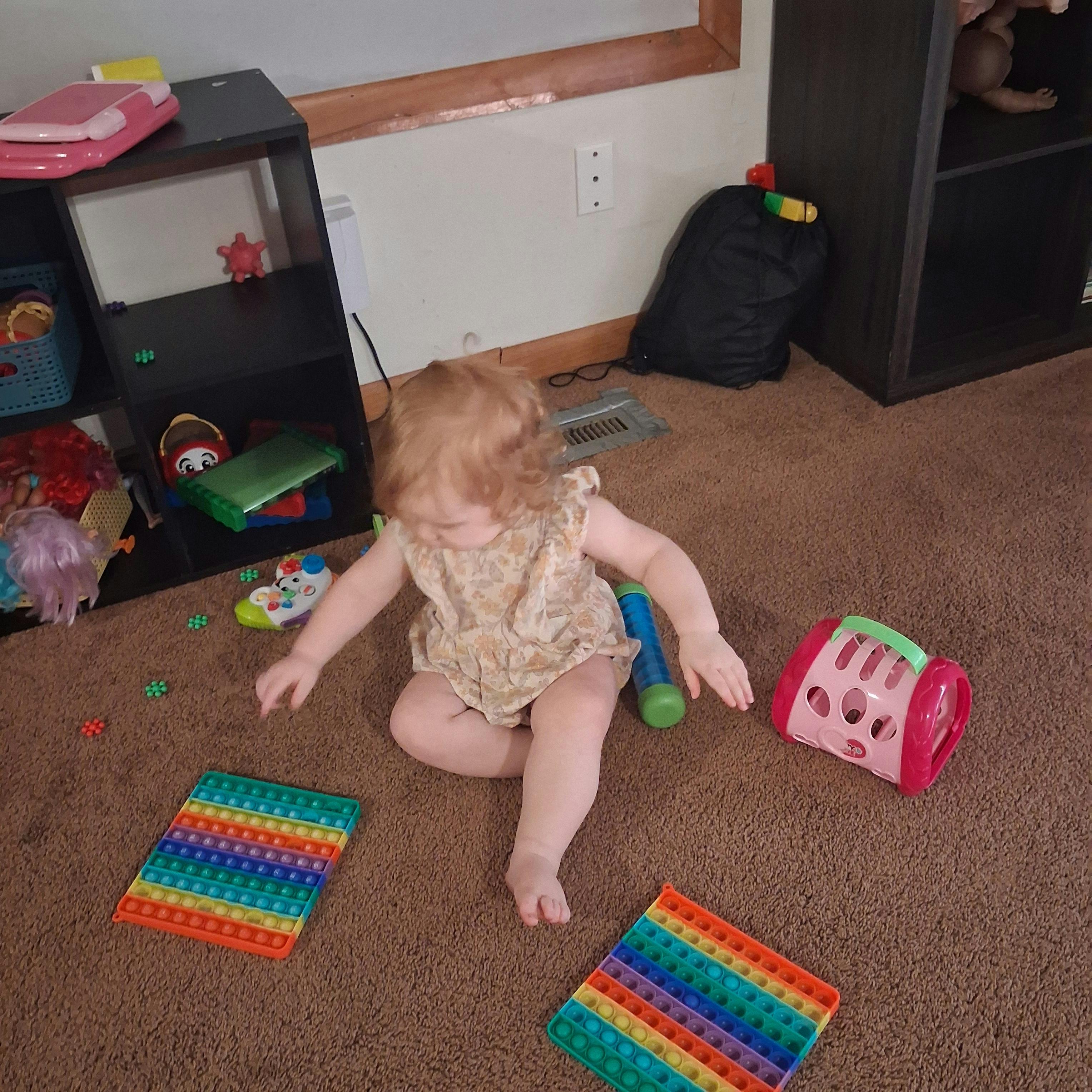 Child sitting on carpeted floor surrounded by various toys