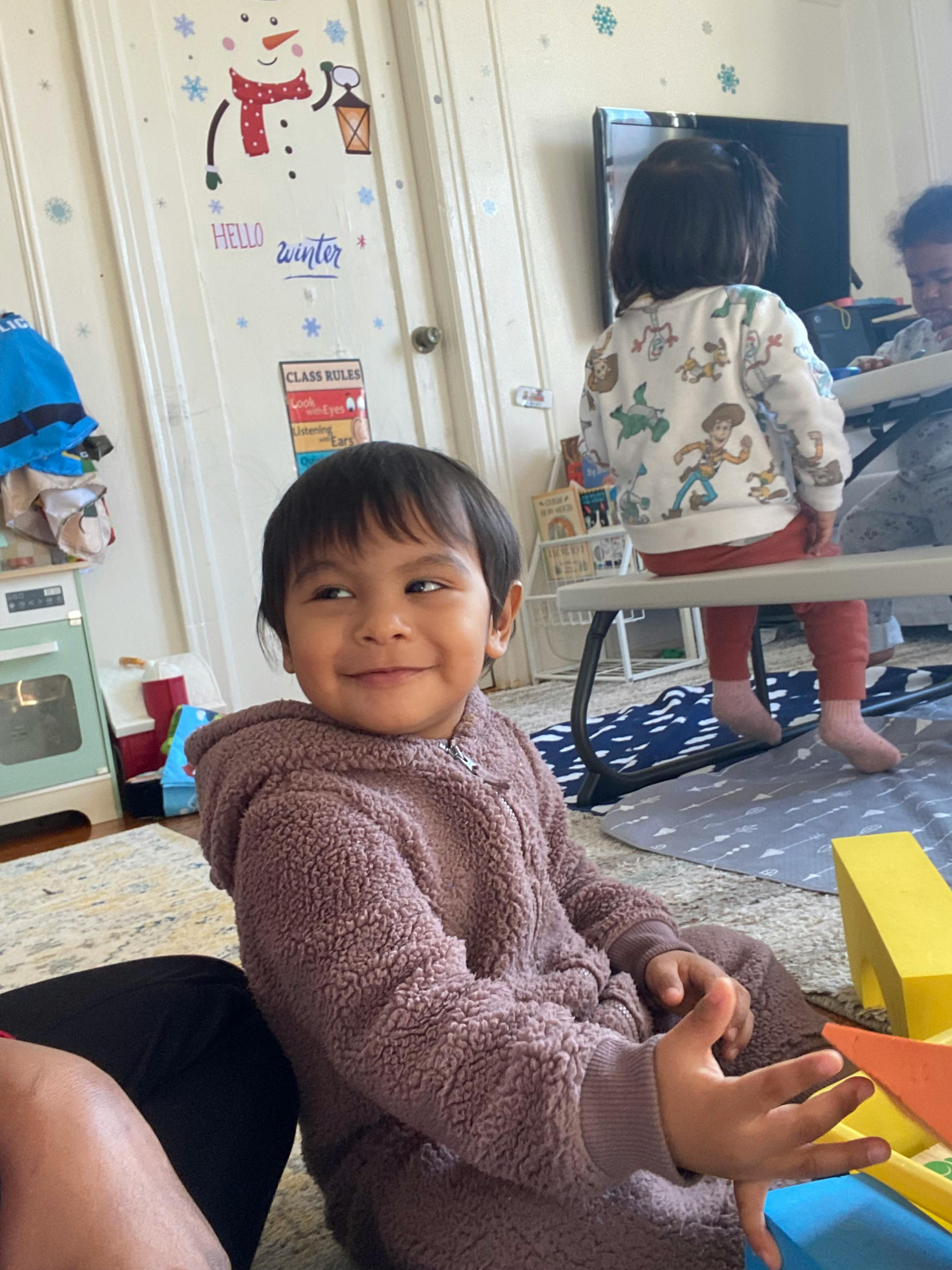 Child in a fuzzy hooded outfit smiling, another child in background