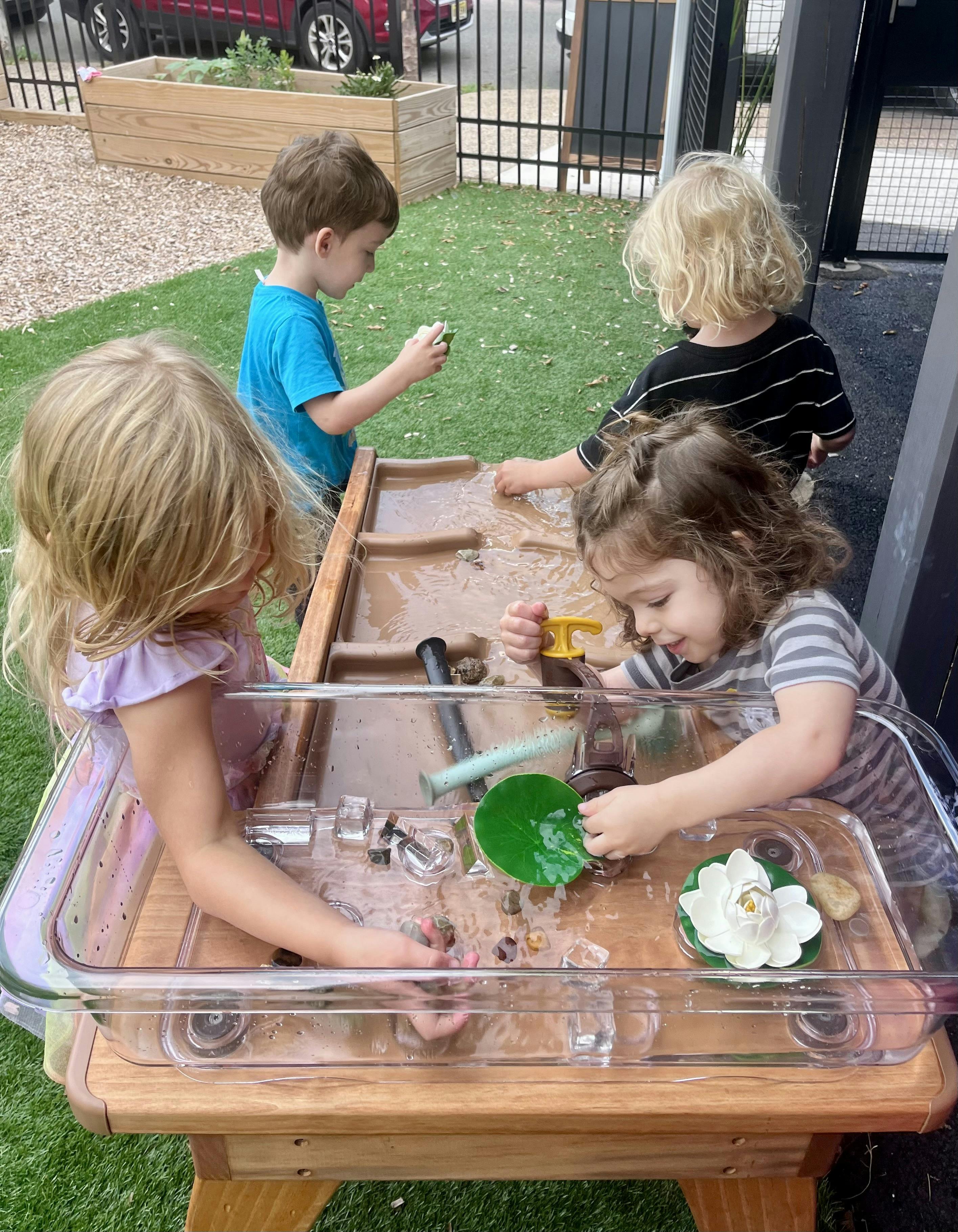 Four children playing with water and toys in a sensory table
