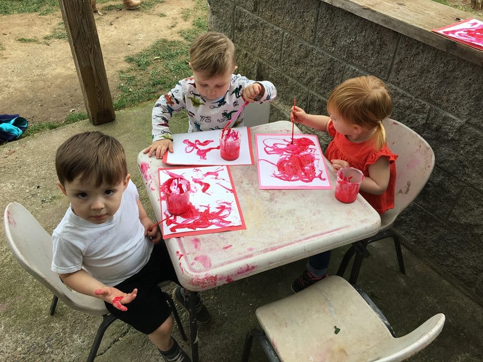 Three children painting with red paint at a table