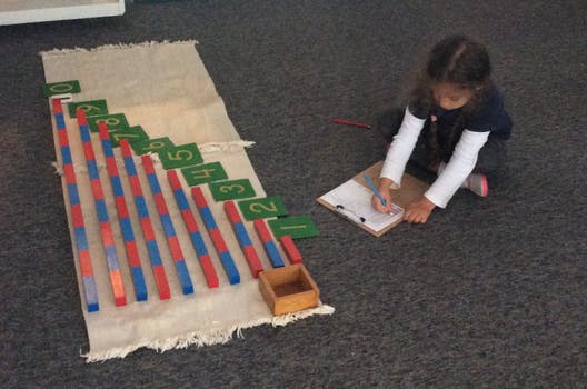 Child writing on a clipboard next to counting rods and number cards