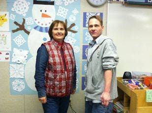 Two people standing in front of a snowman decoration
