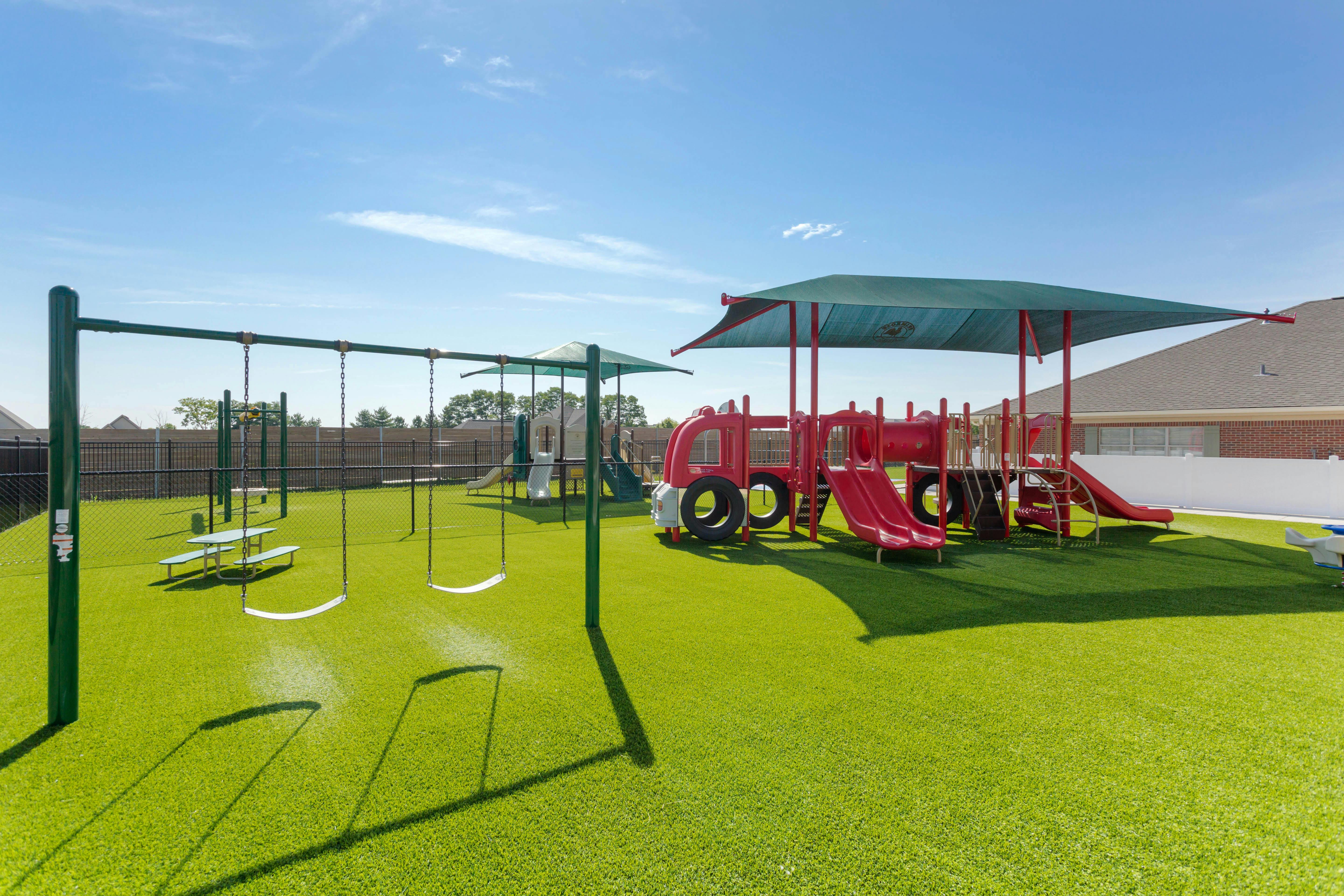 Empty outdoor playground with swings and play structures on green artificial turf