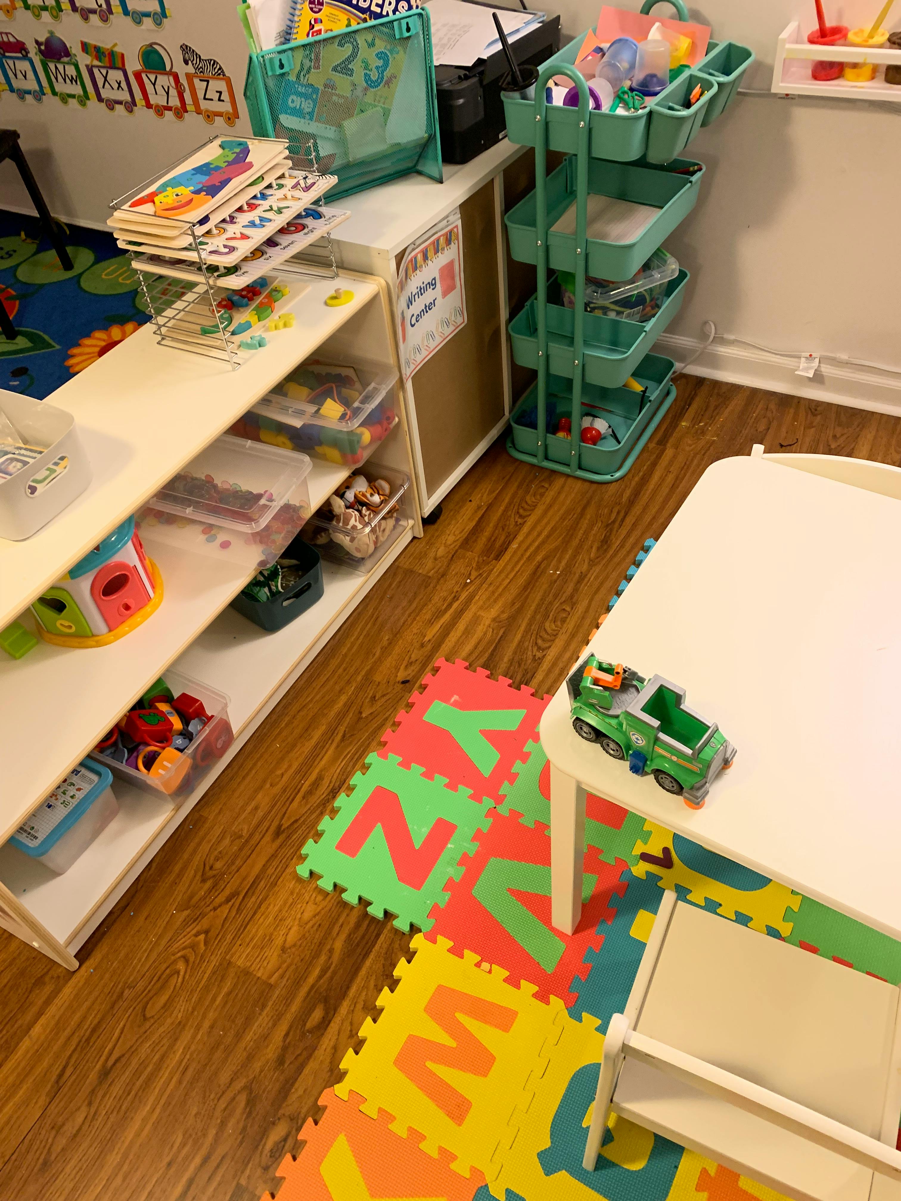 Classroom with shelves of toys, a table, and alphabet floor mats