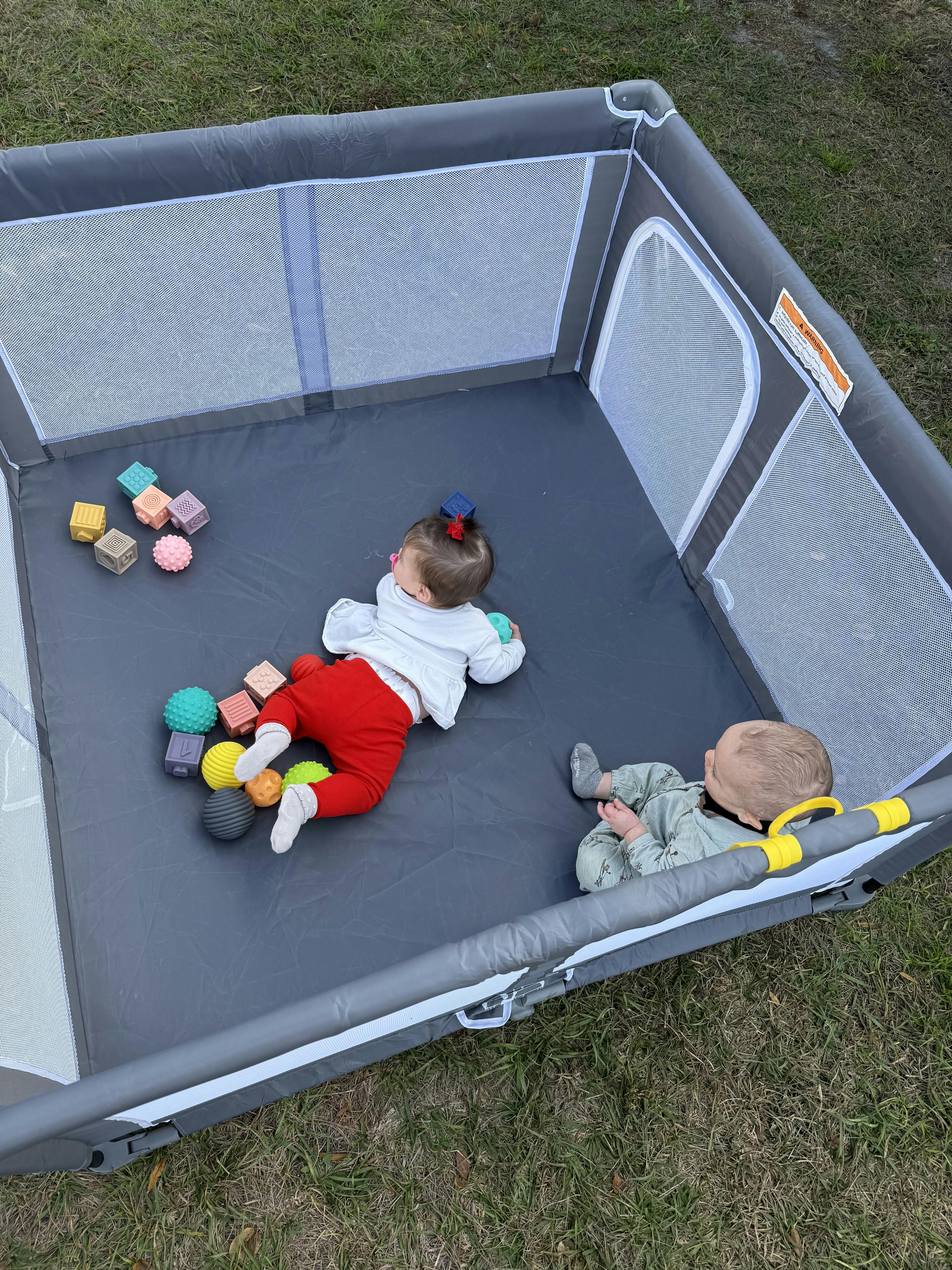 Two children playing with textured blocks and balls in a playpen outdoors