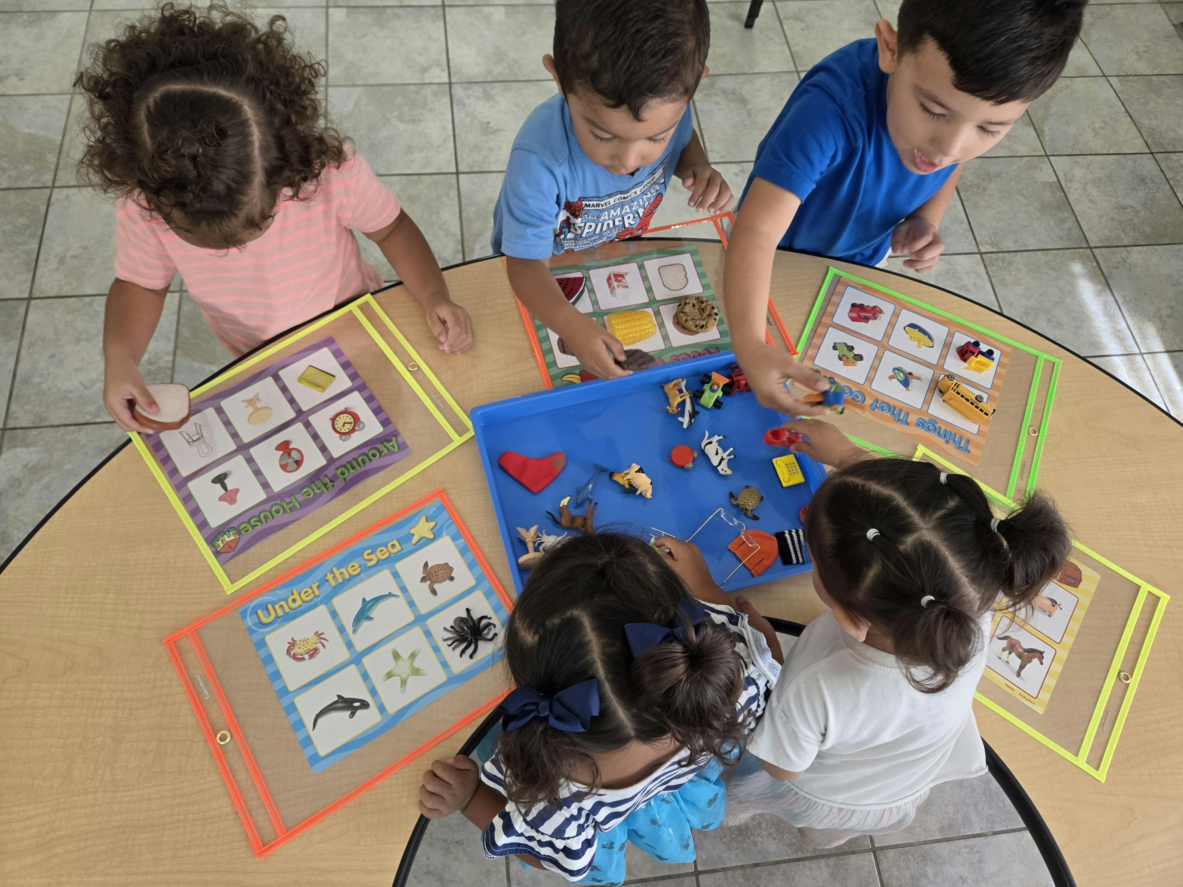 Four children sitting at a circular table sorting small animal and object toys