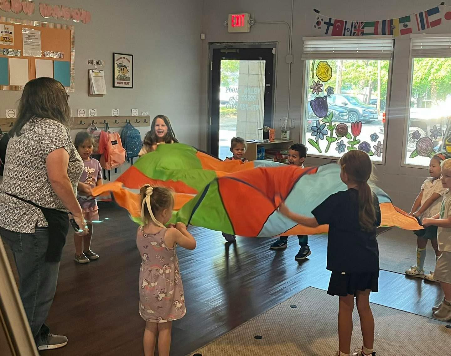 A teacher and children playing with a colorful parachute in a classroom