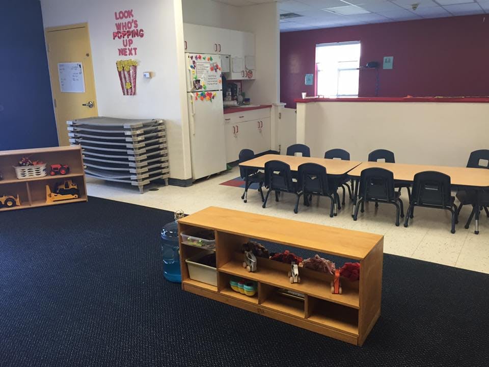 Classroom with small tables and chairs, shelves, and stacked cots