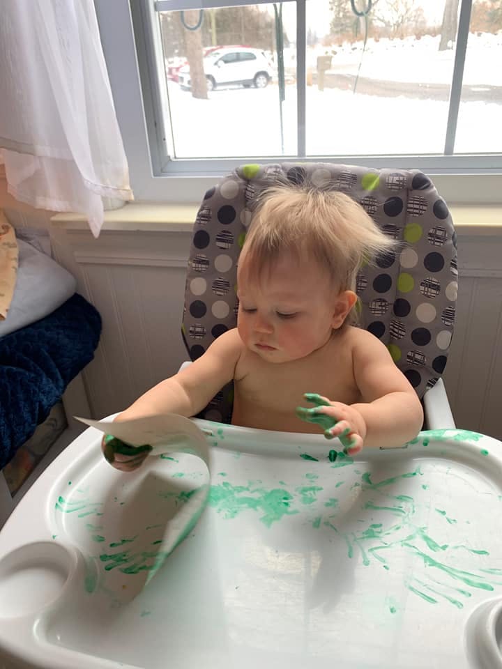 Child in high chair with green paint on hands and tray