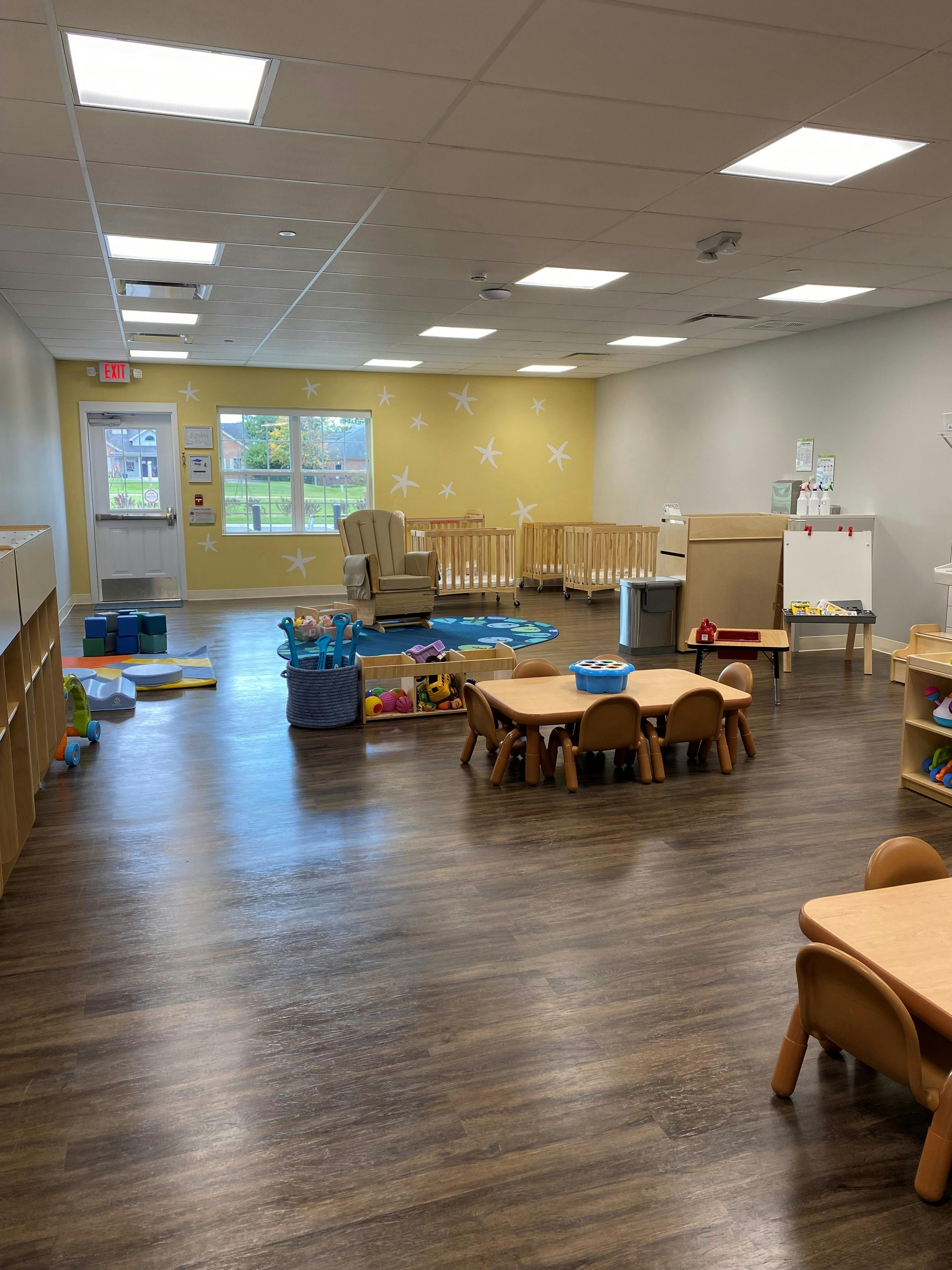 Empty classroom with small tables, chairs, cribs, and toys