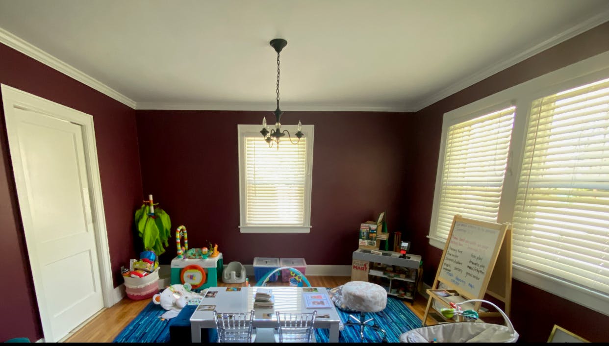 Room with dark red walls, white trim, and a blue rug with toys