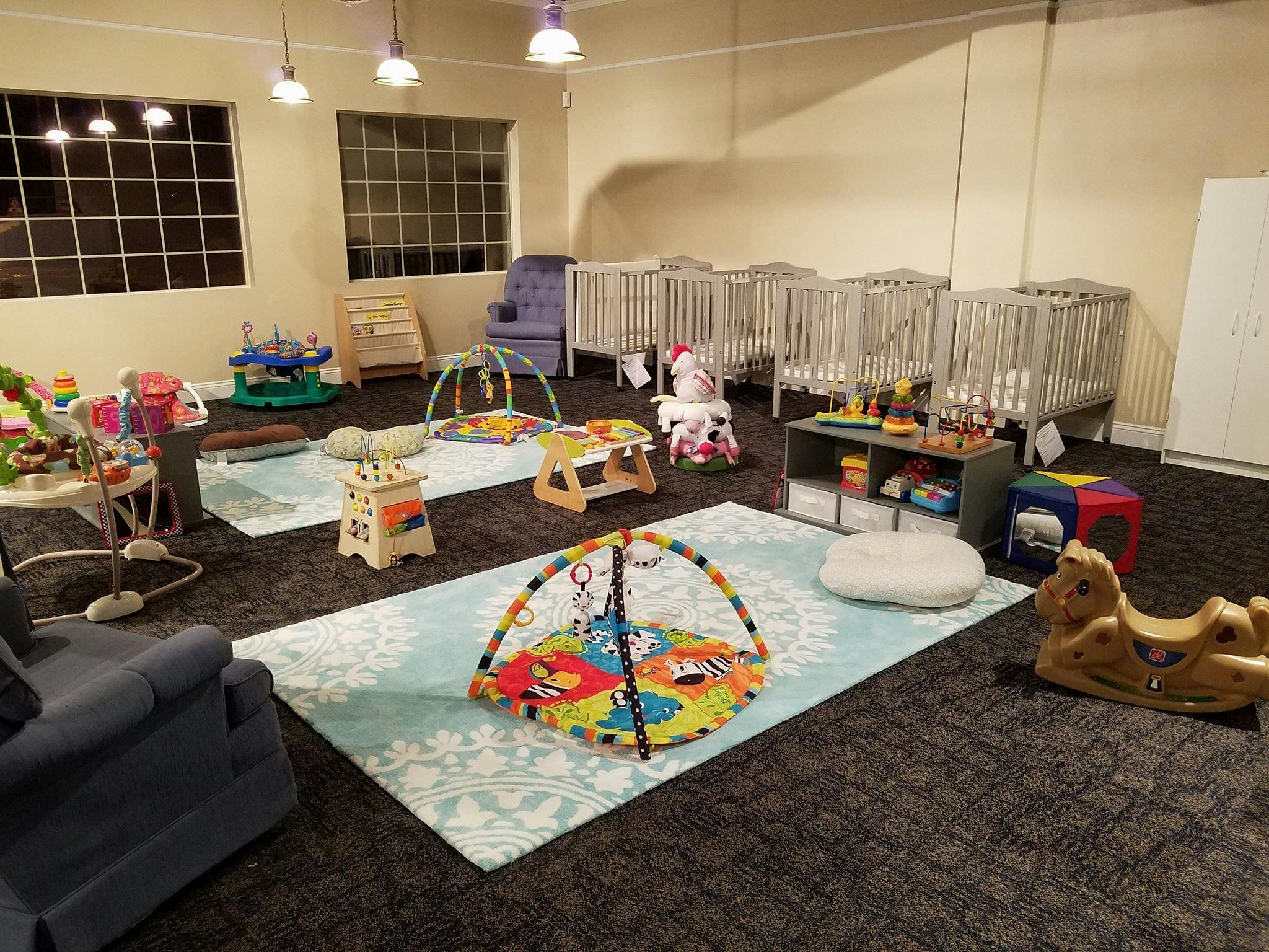 Daycare room with multiple cribs, play mats, and toys