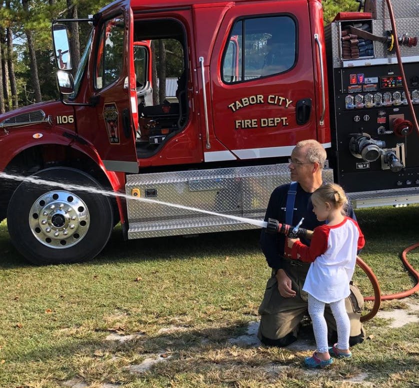 Person and child holding a hose spraying water in front of a fire truck