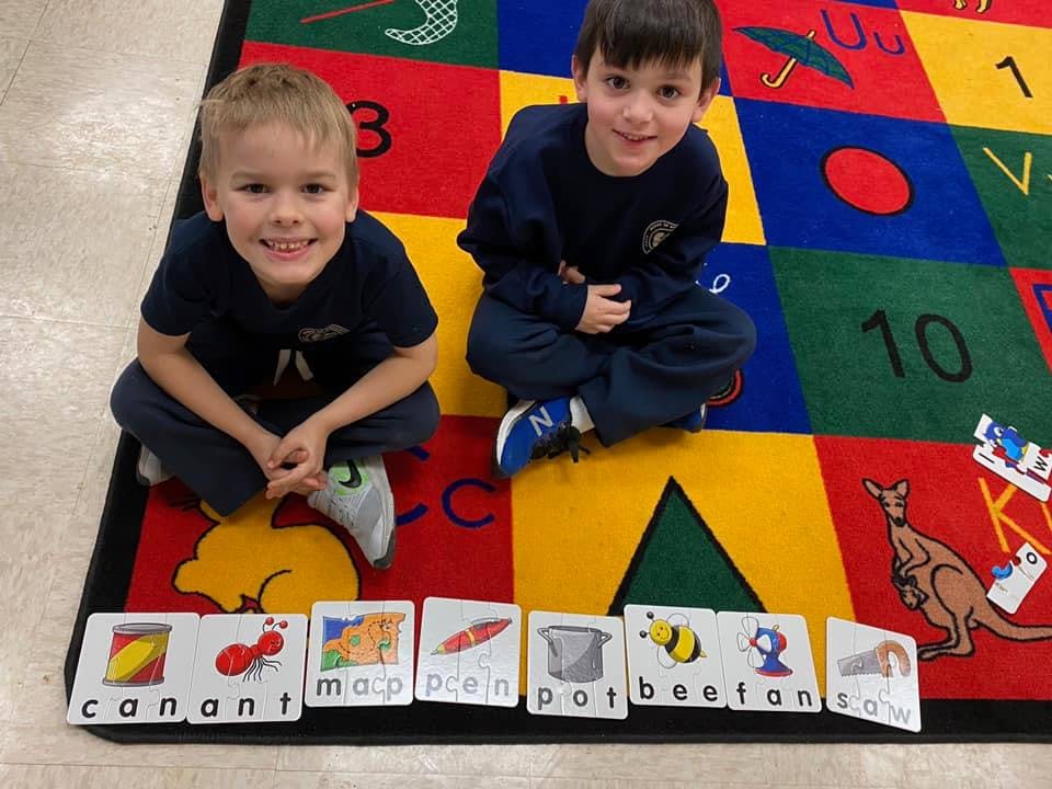 Two children sitting on a colorful rug with word cards in front of them
