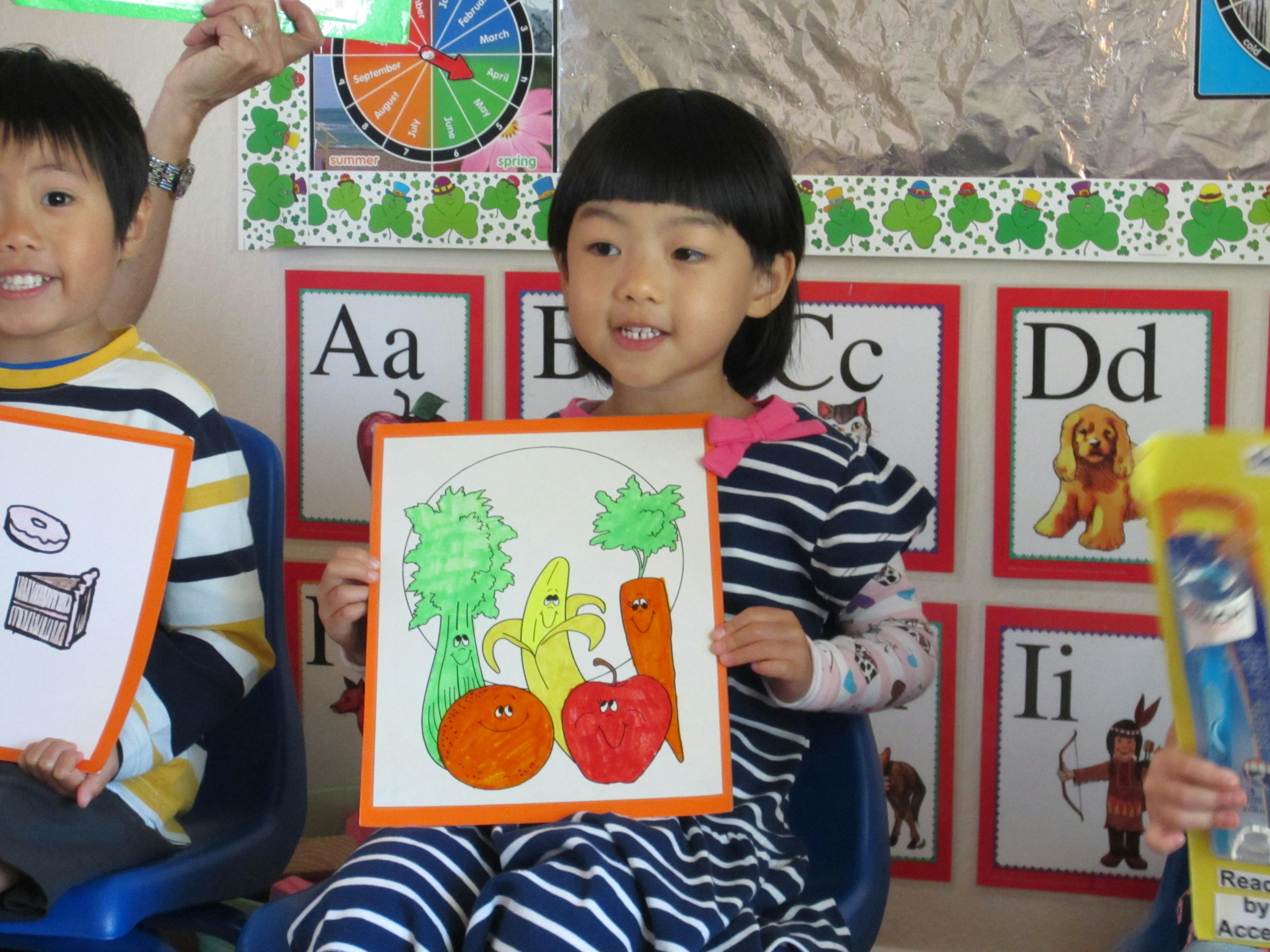 Child holding up a drawing of fruits and vegetables