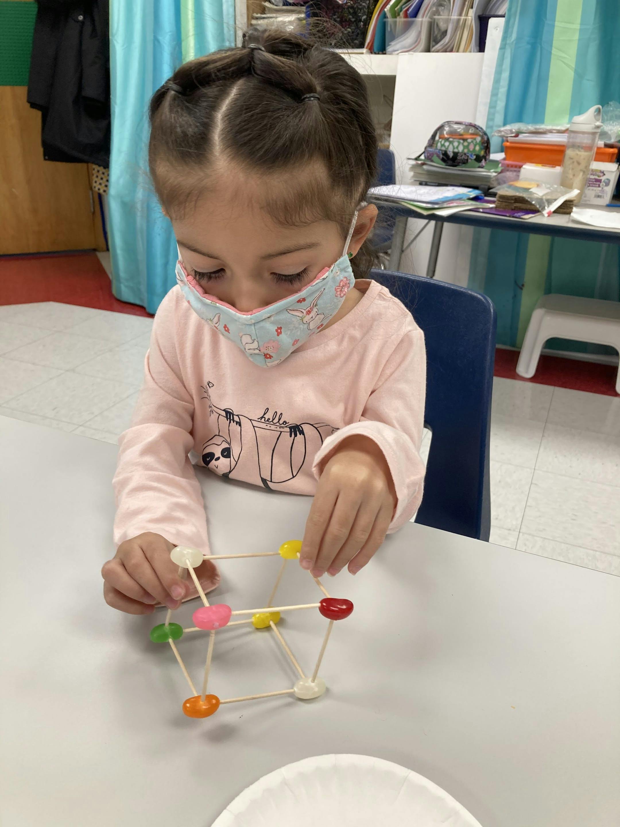 Child in mask building a structure with toothpicks and jelly beans
