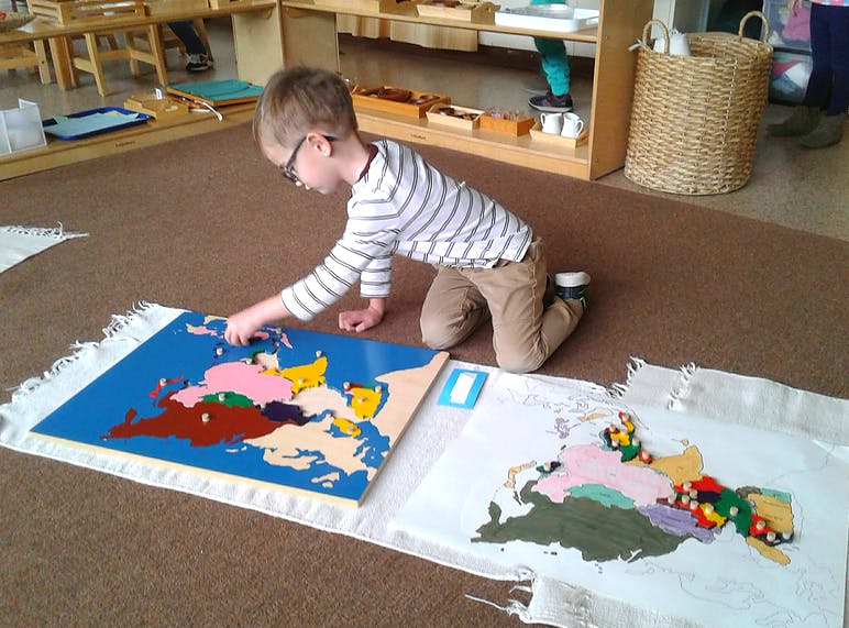 Child kneeling on floor, working on a colorful map puzzle