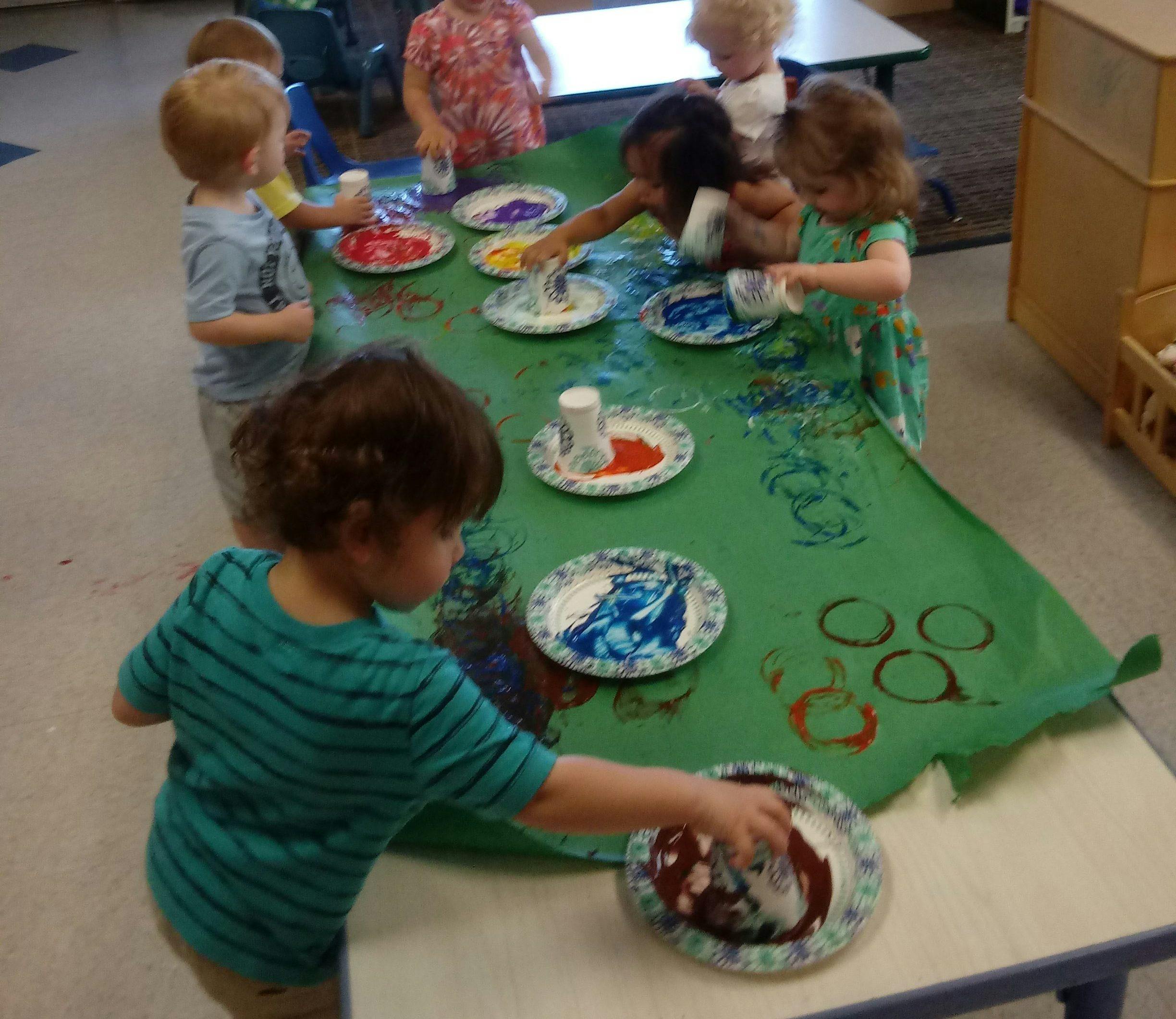Children finger painting at a table in a classroom