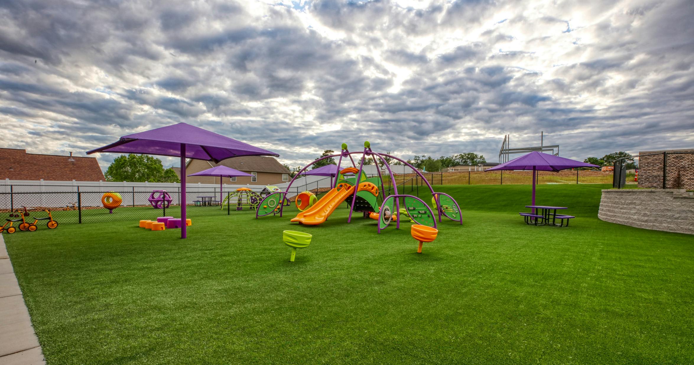 A colorful playground with slides and climbing structures on green artificial turf