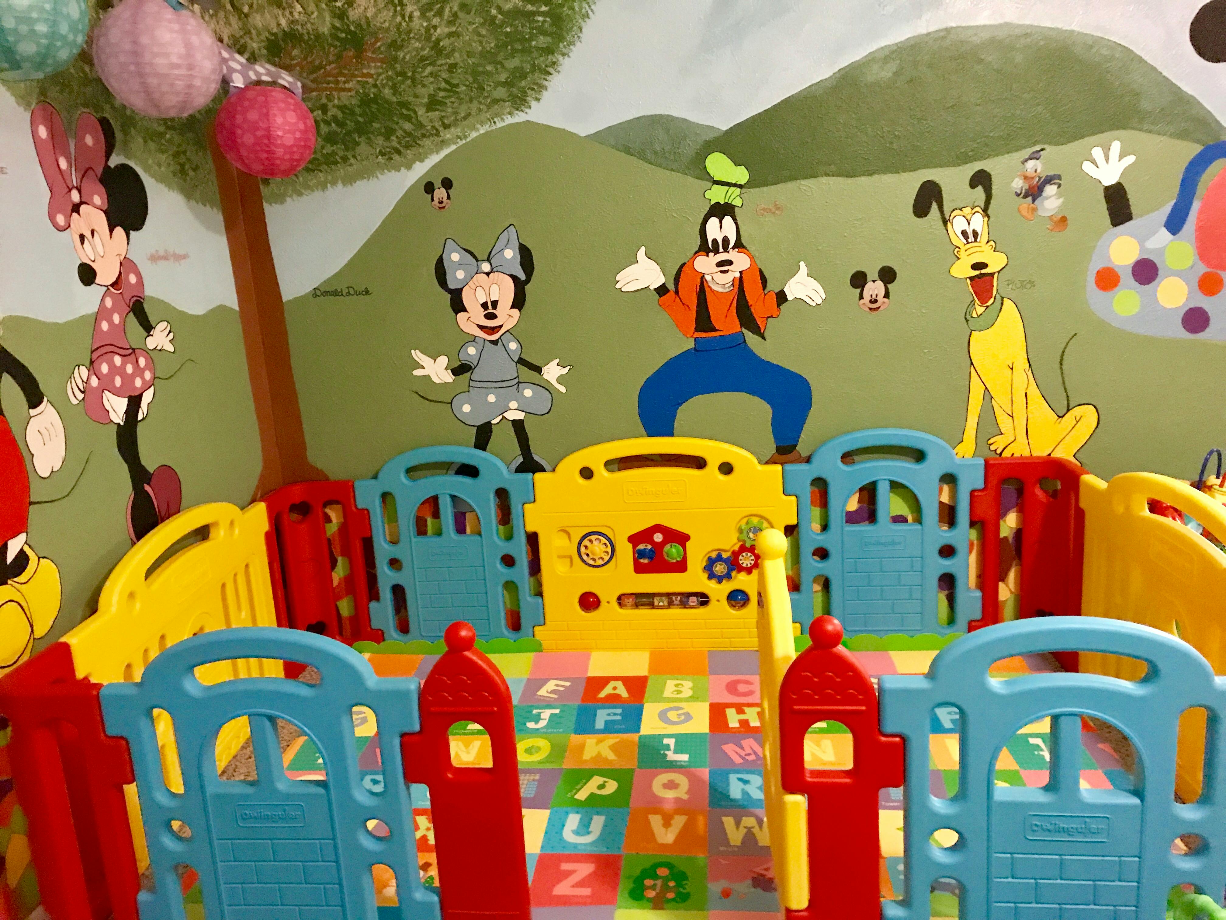 Playpen with alphabet mat and cartoon character cutouts on the wall