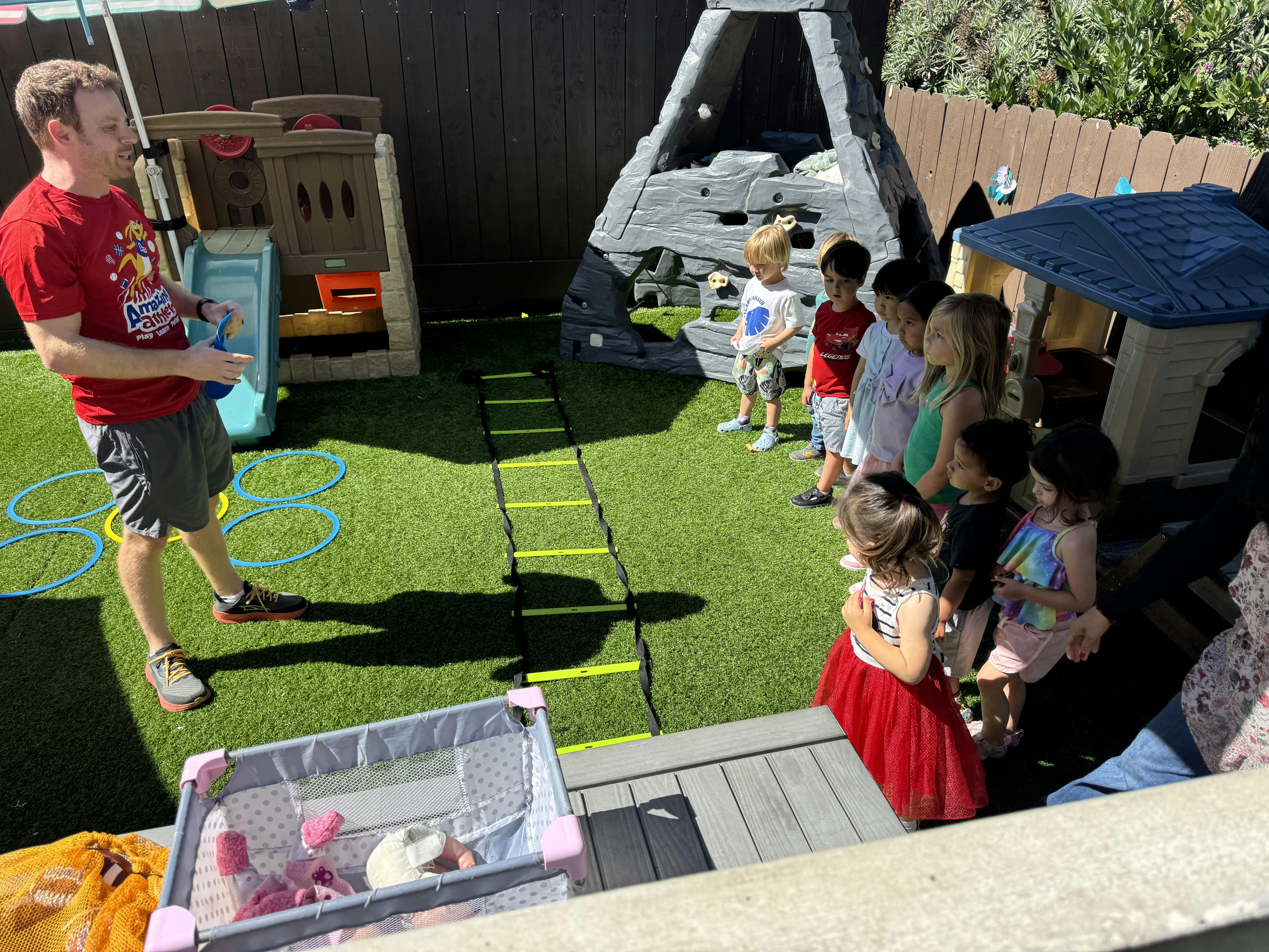 Adult leading a group of children in an outdoor activity on artificial grass