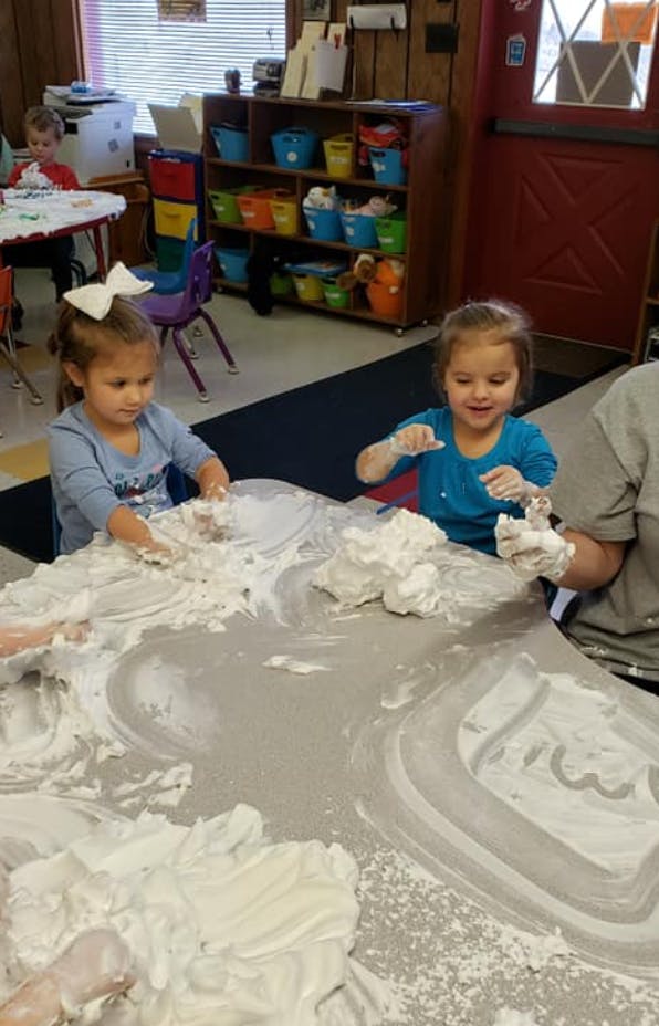 Two children playing with shaving cream on a table in a classroom