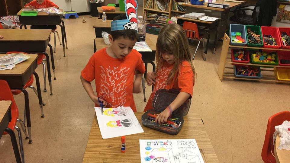 Two children doing crafts at a desk in a classroom