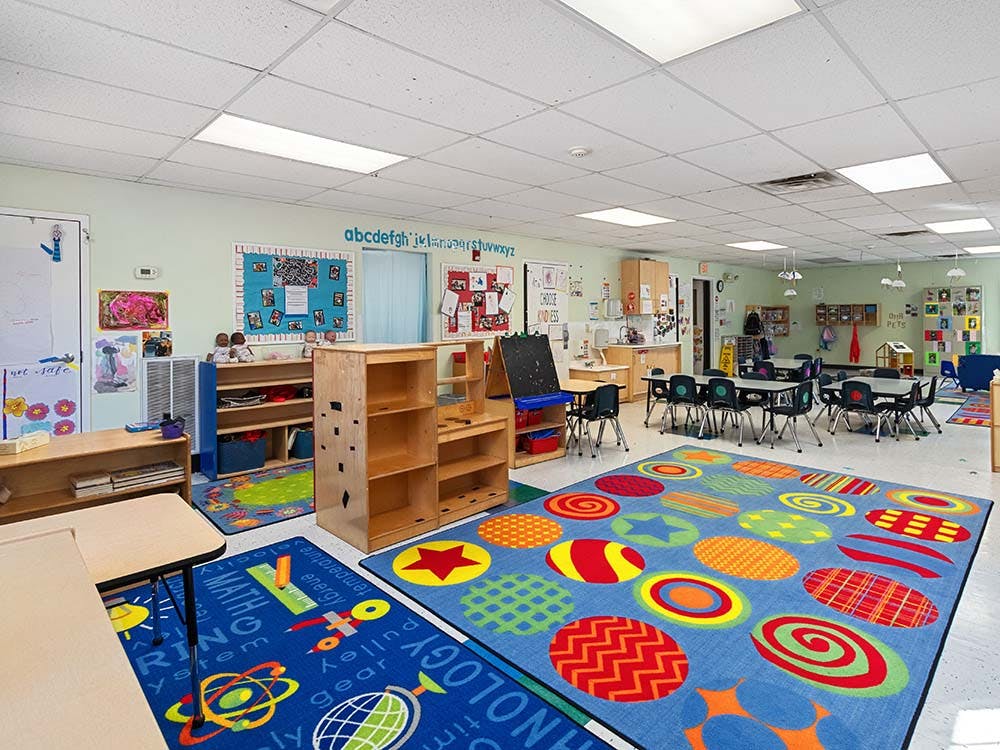 Classroom with colorful rugs, small tables and chairs, shelves, and learning materials