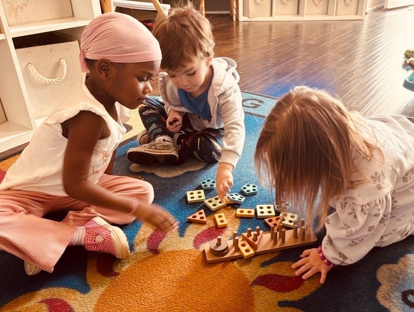 Three children playing with wooden blocks and a puzzle on a colorful rug