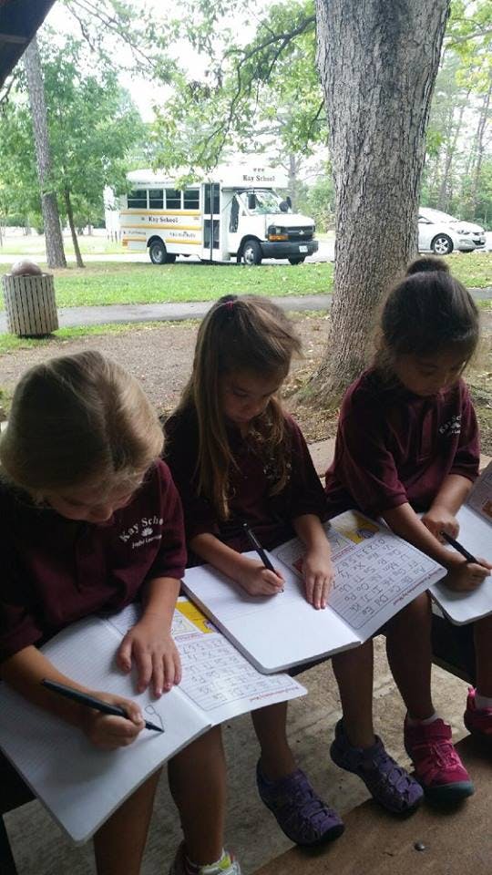 Three children writing in notebooks outdoors