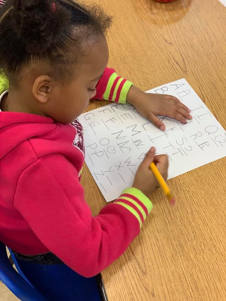 Child writing letters on a piece of paper with a pencil
