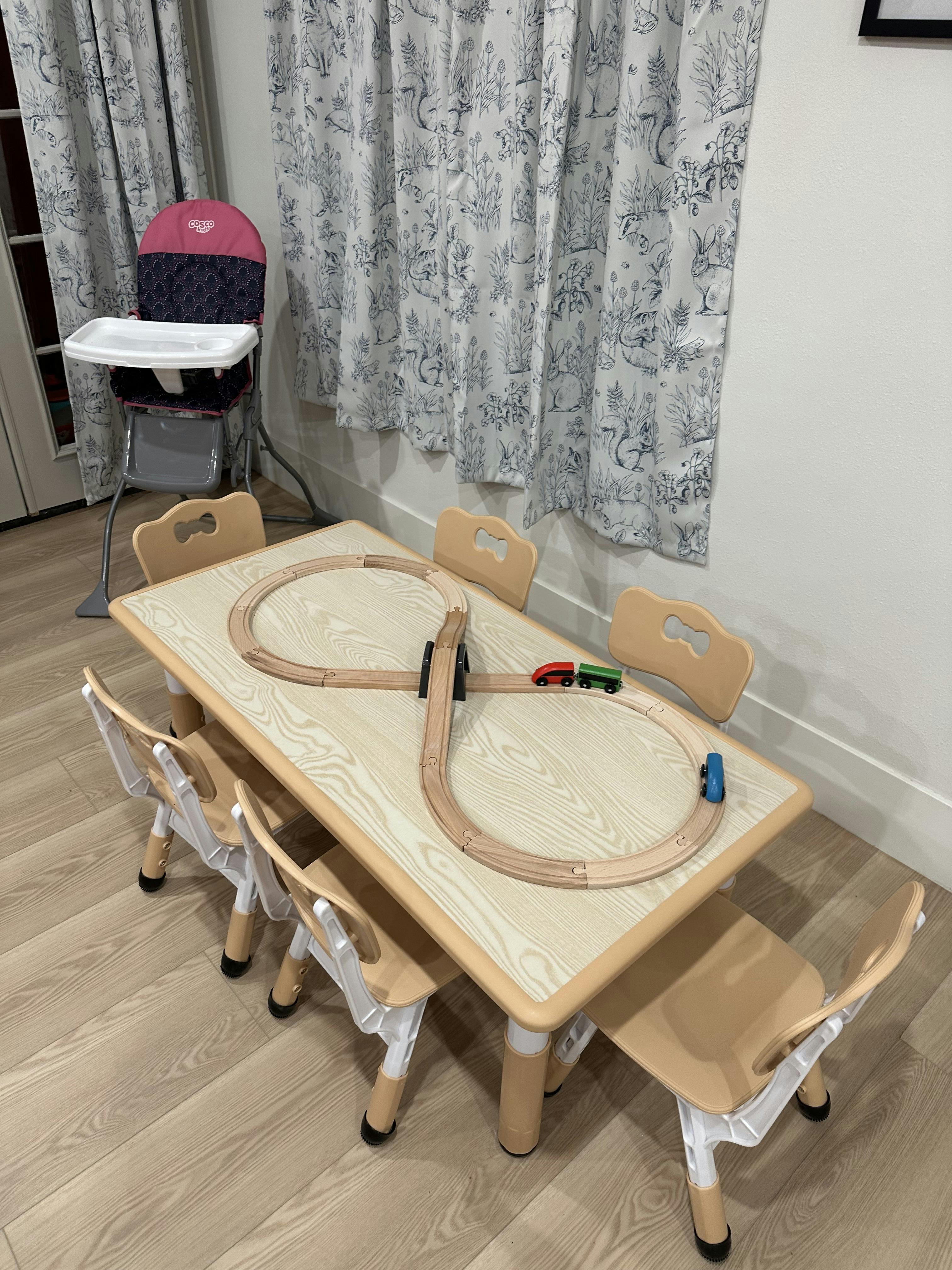 Wooden train set with two small trains on a table with several small chairs