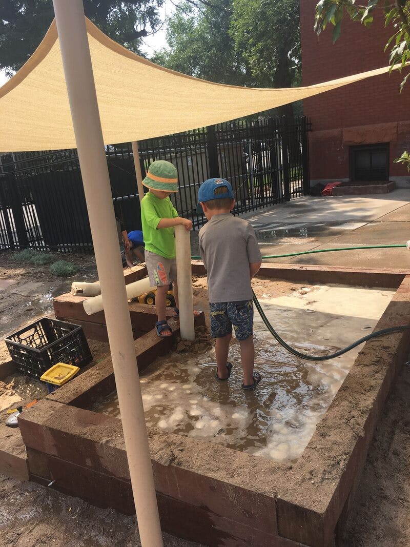 Two children playing in a sandbox with water