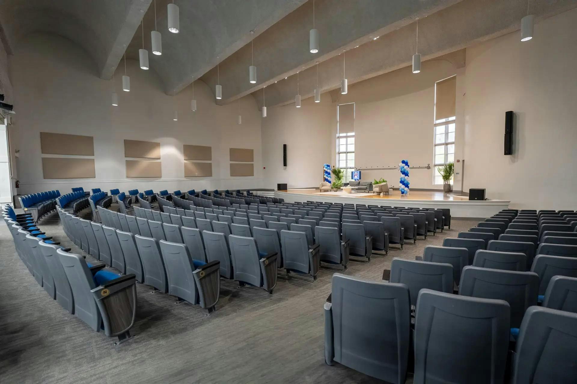 An empty auditorium with rows of seating facing a stage decorated with balloons