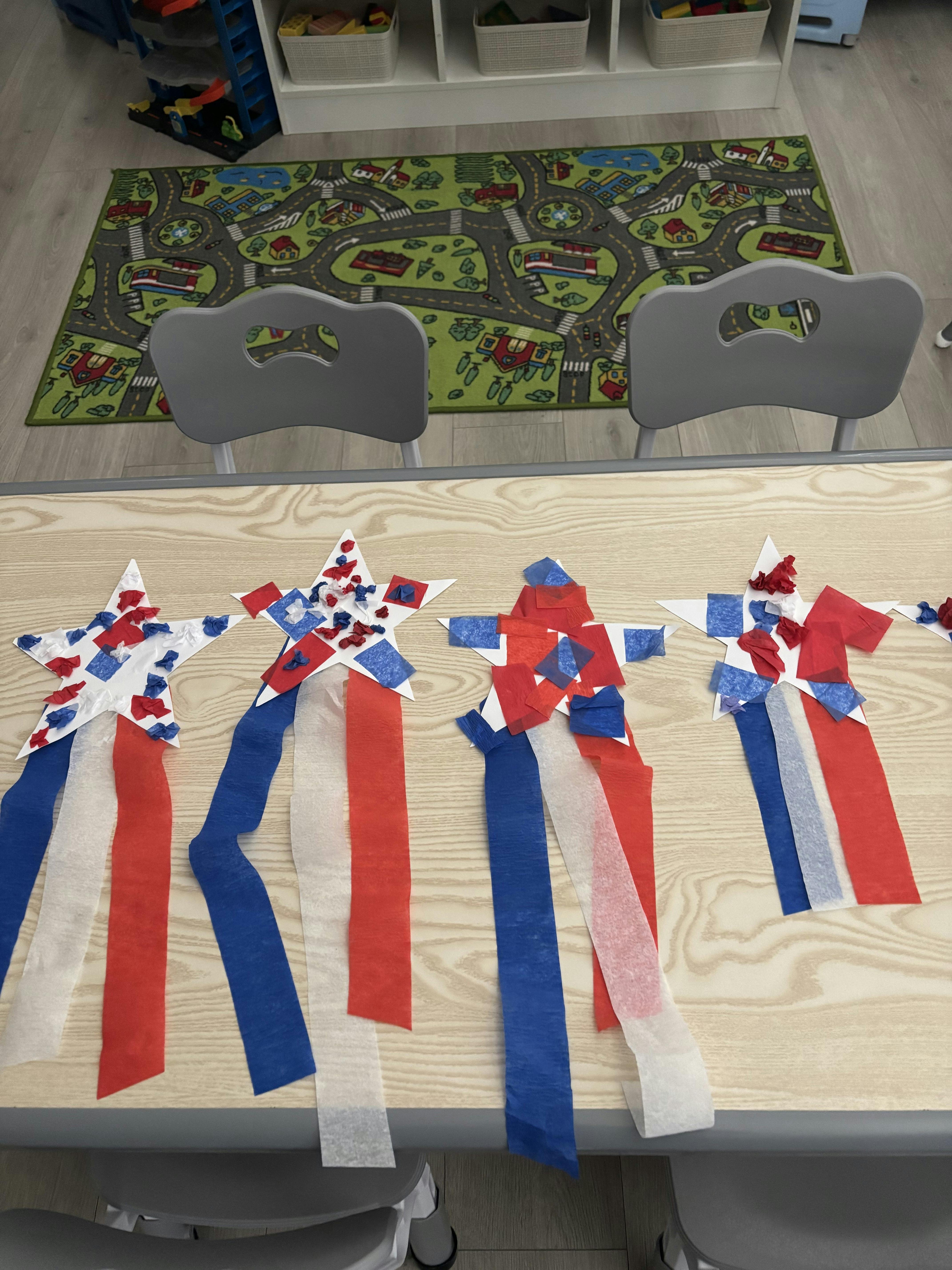 Four handmade star crafts with red, white, and blue streamers on a classroom table