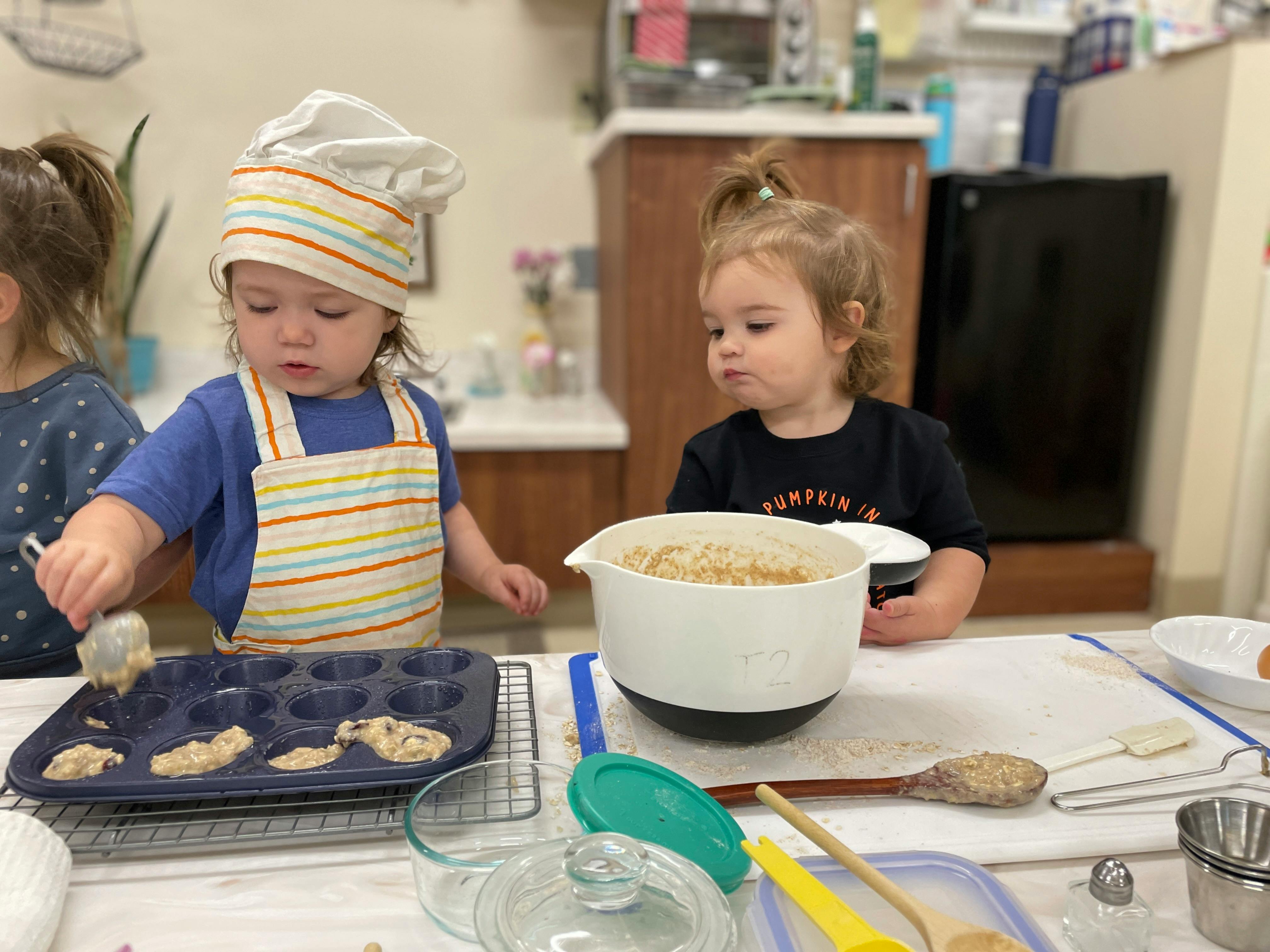 Child in chef hat and apron putting batter into a muffin tin