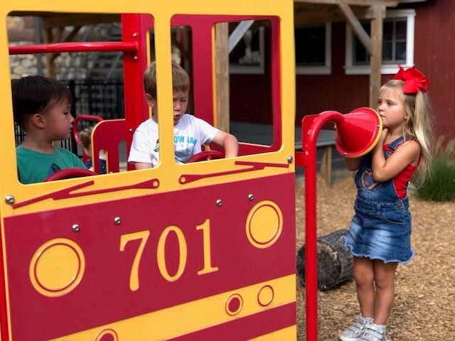 Child speaking into a red play megaphone, two children in a play train