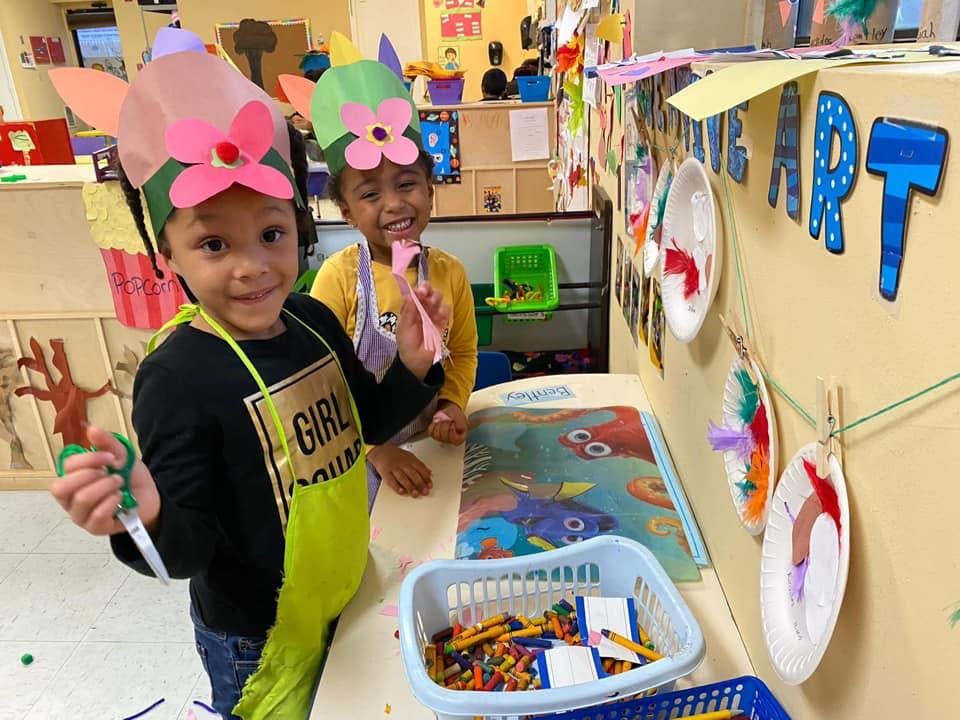 Two children wearing paper hats and aprons, one holding scissors
