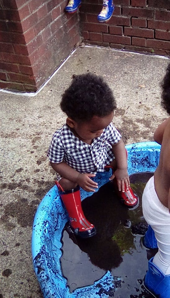 Child in a plaid shirt and red boots playing in a blue wading pool