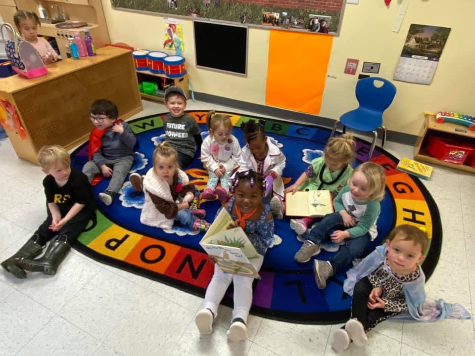 Children sitting on a colorful rug, some reading books