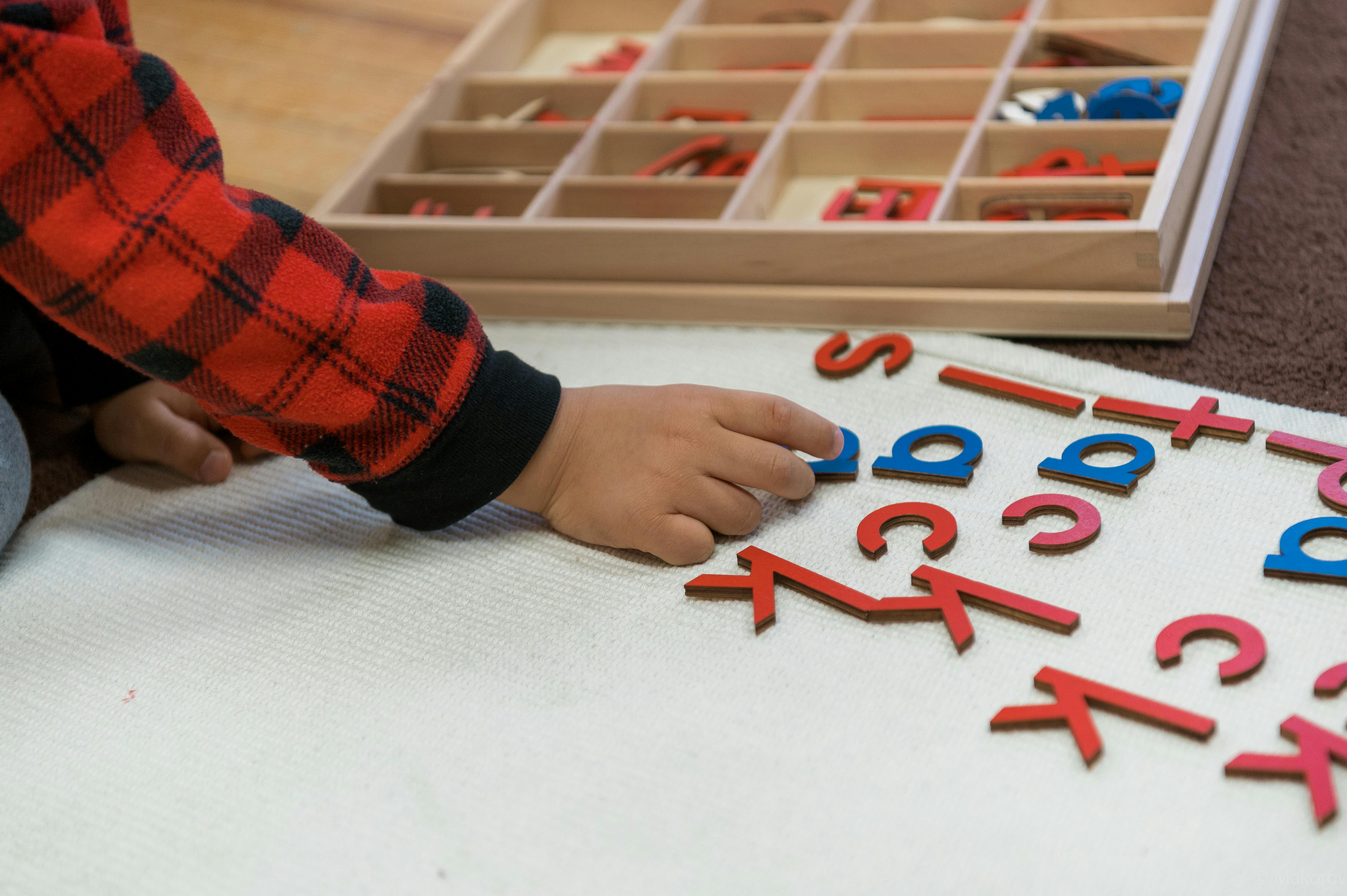 Child's hand arranging letter cutouts on a white surface