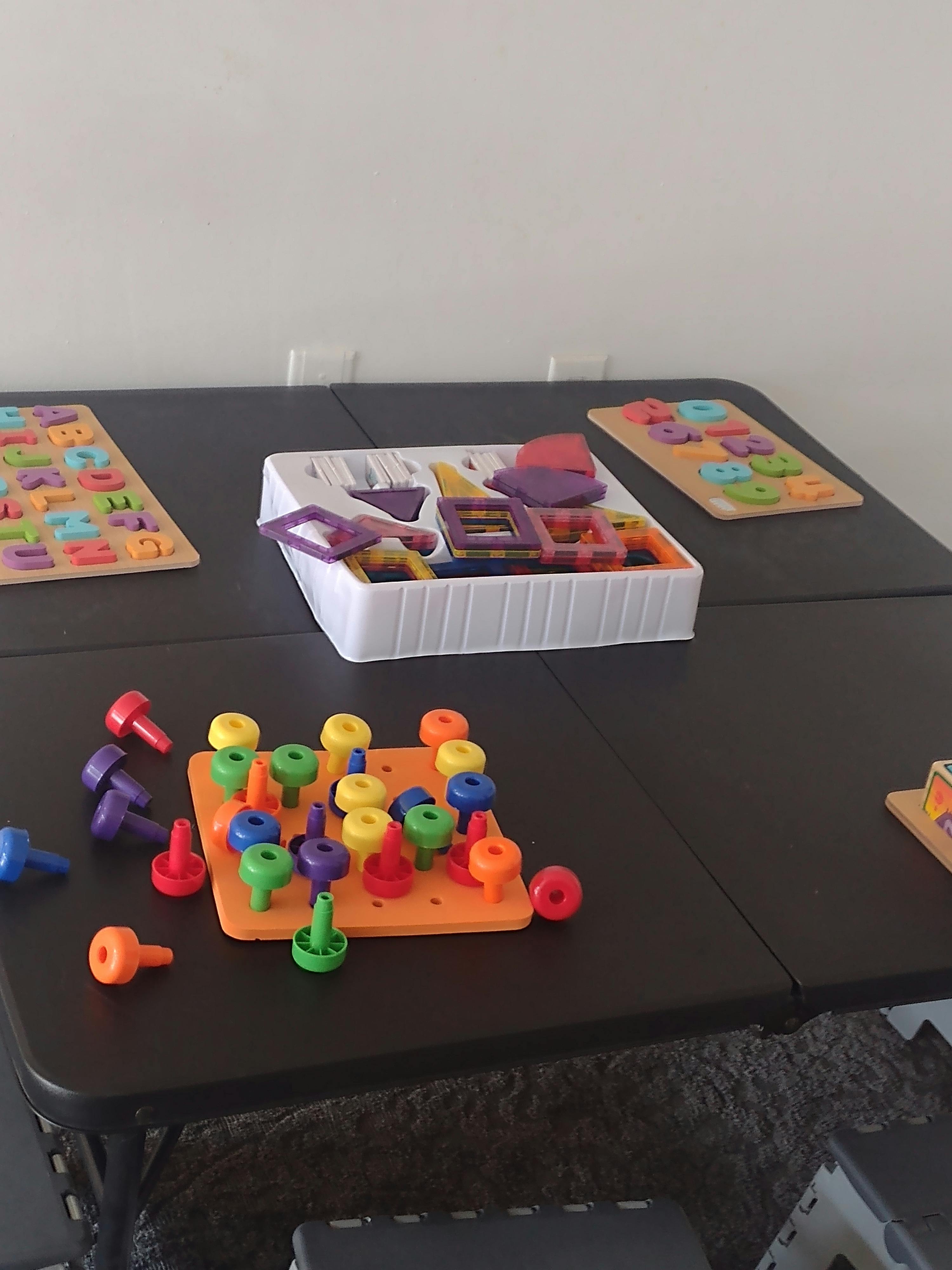 Table with colorful children's learning toys, including a pegboard and alphabet puzzles