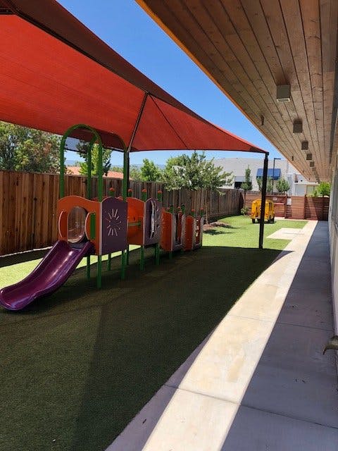 Playground with a slide and climbing structure under a red shade sail