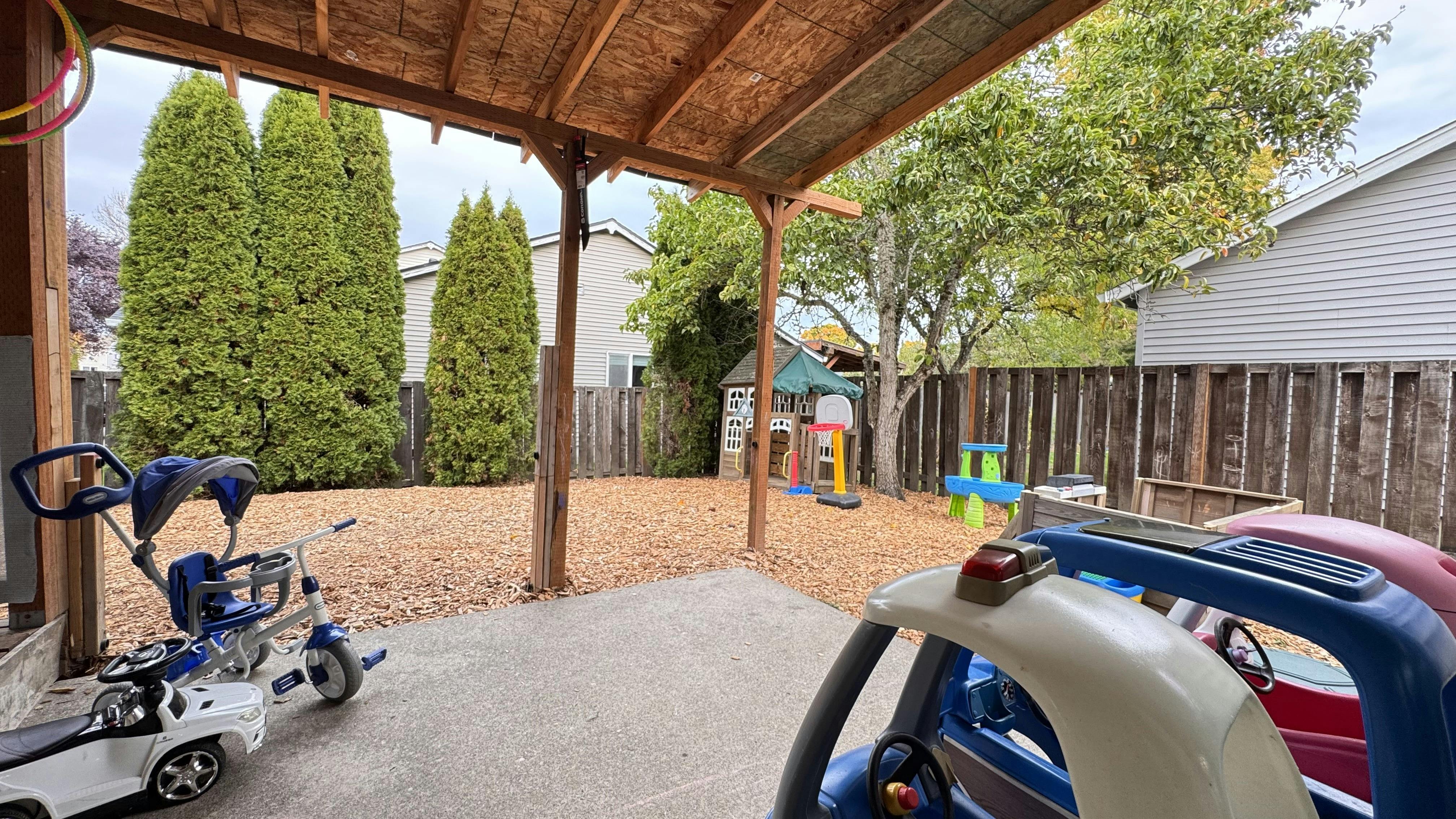 Covered patio with children's ride-on toys and a backyard play area