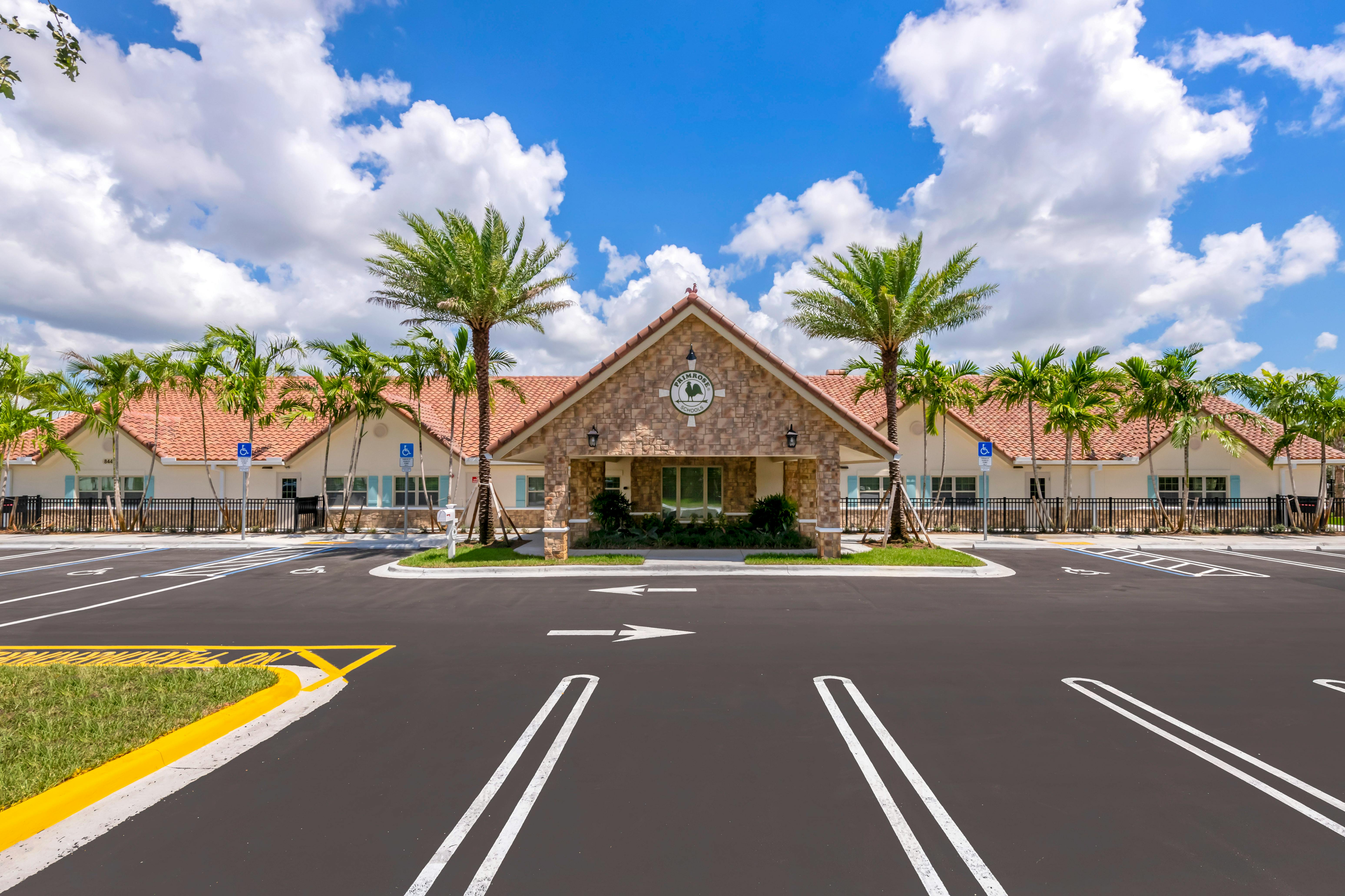 Exterior view of a school building with a large parking lot and palm trees