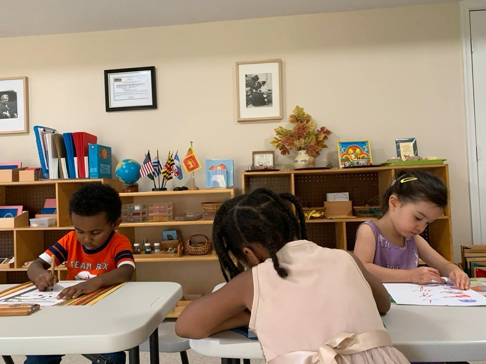 Three children drawing at tables in a classroom