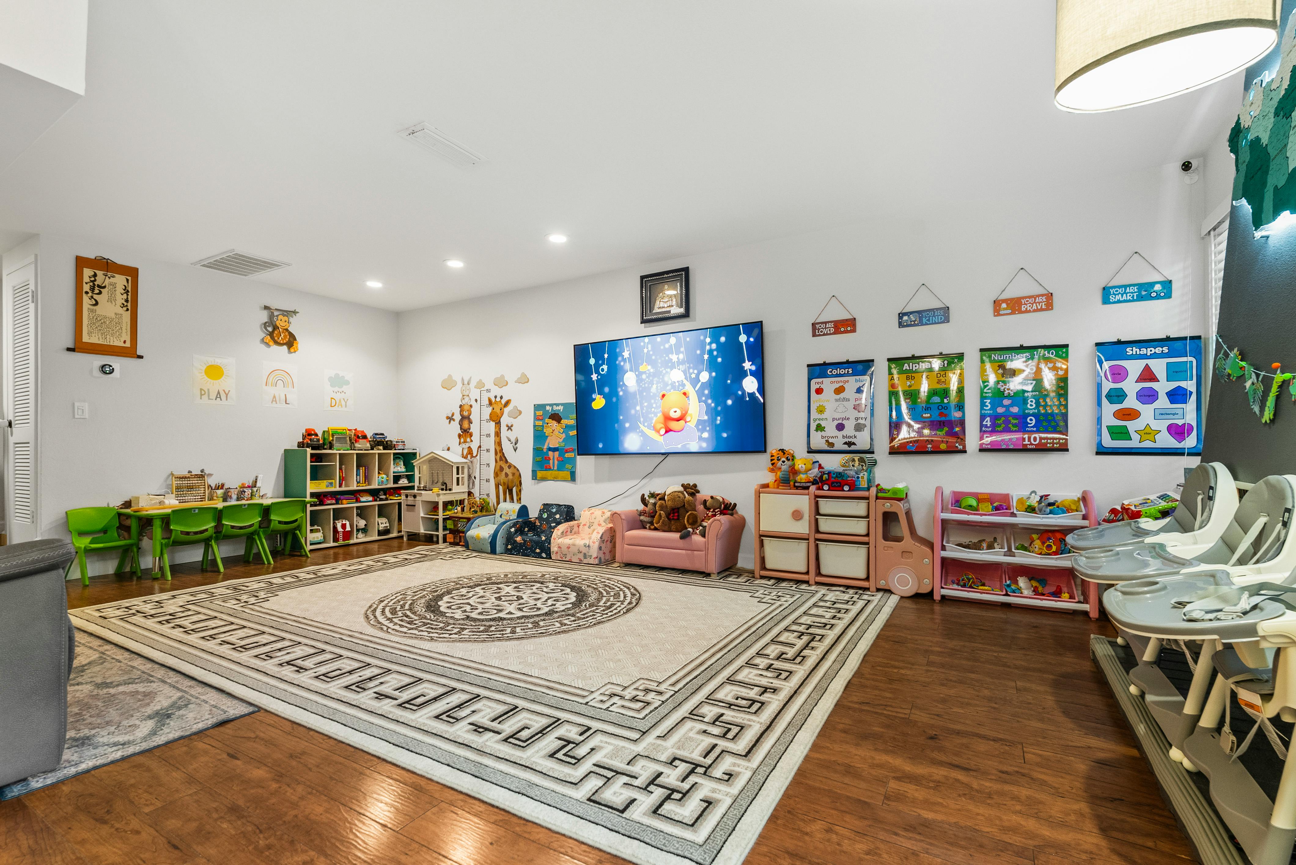 A children's play room with a large rug, small tables and chairs, and a TV