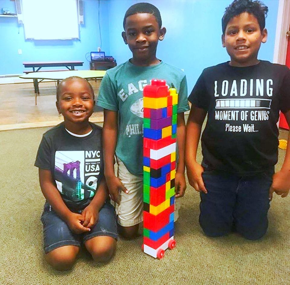 Three children standing and kneeling around a tall stack of colorful building blocks